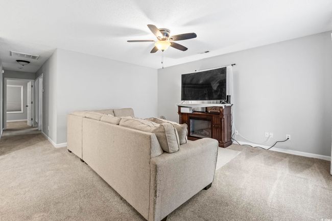 Living area with light colored carpet, a ceiling fan, and a fireplace | Image 4
