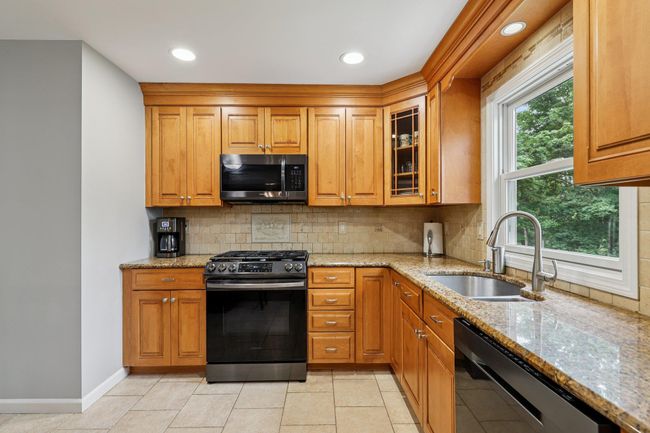 Kitchen with appliances with stainless steel finishes, light stone counters, glass insert cabinets, tasteful backsplash, and recessed lighting | Image 10