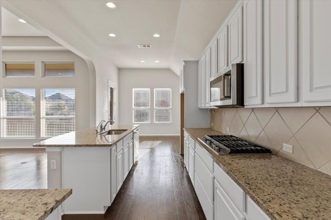 Kitchen with light stone counters, white cabinets, recessed lighting, a kitchen island with sink, and stainless steel appliances | Image 6
