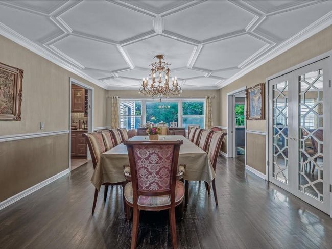 Dining space featuring dark wood-style flooring, french doors, a chandelier, coffered ceiling, and crown molding | Image 6