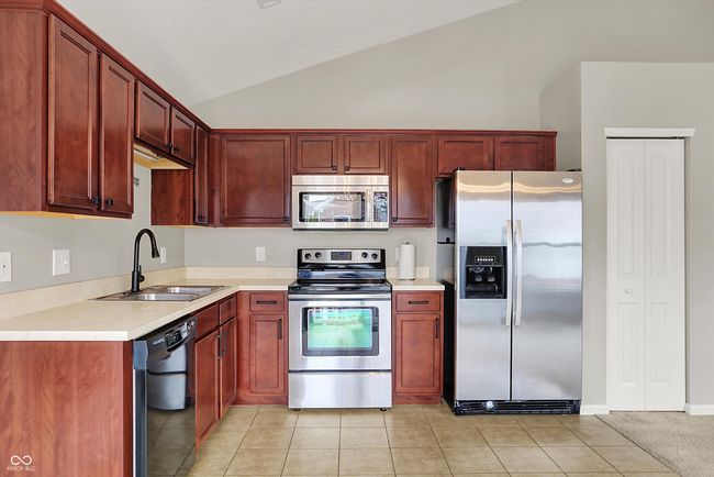kitchen featuring appliances, lofted ceiling, light countertops, light tile patterned flooring, and reddish brown cabinets | Image 15