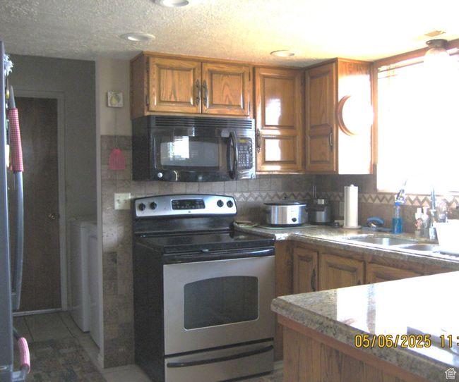 Kitchen featuring brown cabinetry, a sink, black microwave, stainless steel range with electric stovetop, and tasteful backsplash | Image 18