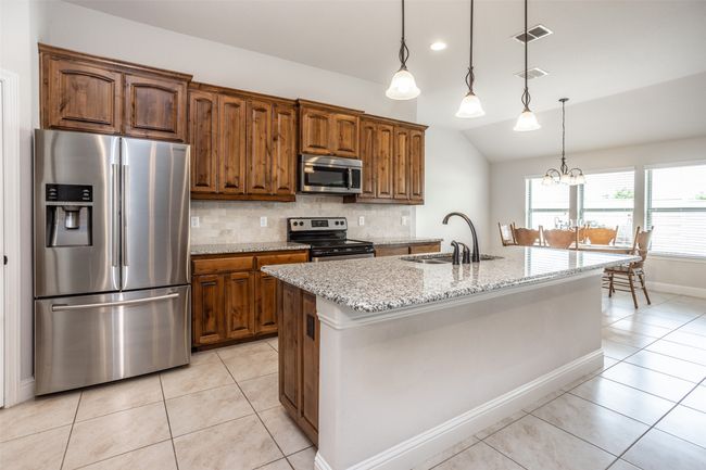 Kitchen featuring appliances with stainless steel finishes, lofted ceiling, light tile patterned flooring, tasteful backsplash, and light stone counters | Image 15