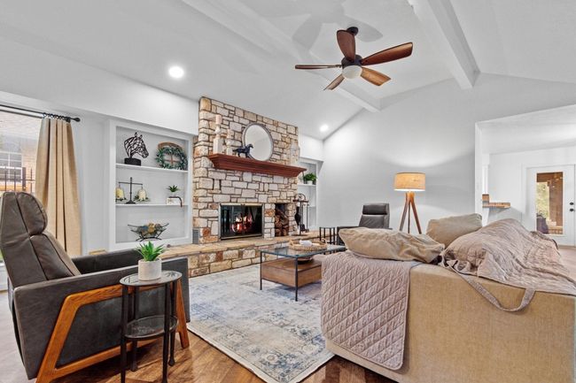 Living room featuring light wood-type flooring, ceiling fan, a stone fireplace, and built in shelves | Image 8