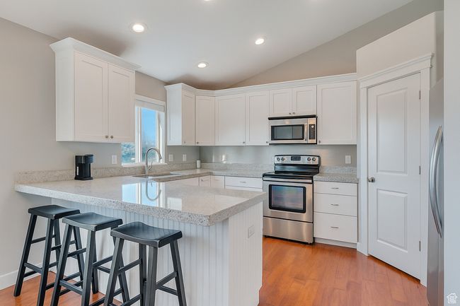 Kitchen with stainless steel appliances, a peninsula, white cabinetry, a breakfast bar, and vaulted ceiling | Image 6