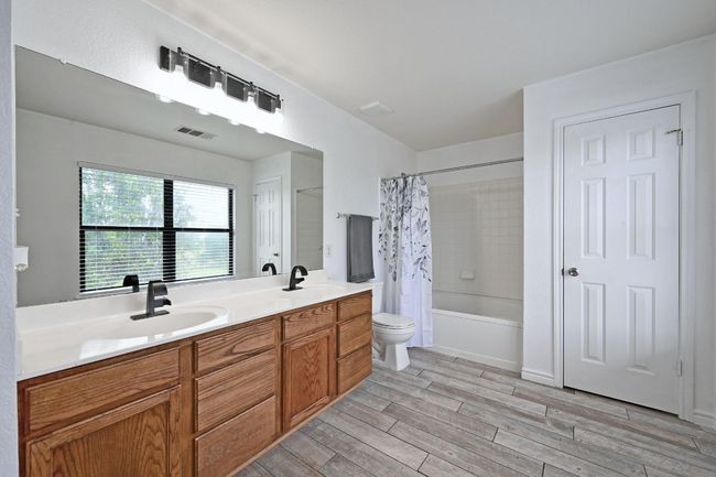 Bathroom with wood finished floors, shower / bath combo with shower curtain, toilet, and double vanity | Image 25