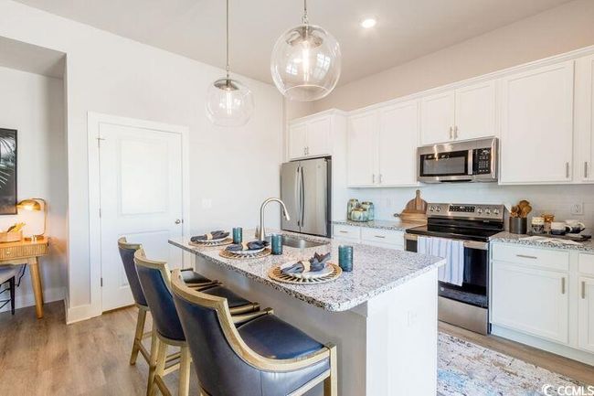 Kitchen featuring light stone countertops, a kitchen island with sink, a sink, appliances with stainless steel finishes, and white cabinetry | Image 8