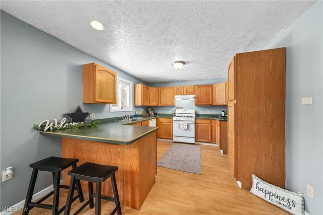 Kitchen with white gas range, a kitchen breakfast bar, a textured ceiling, and light wood-type flooring | Image 6