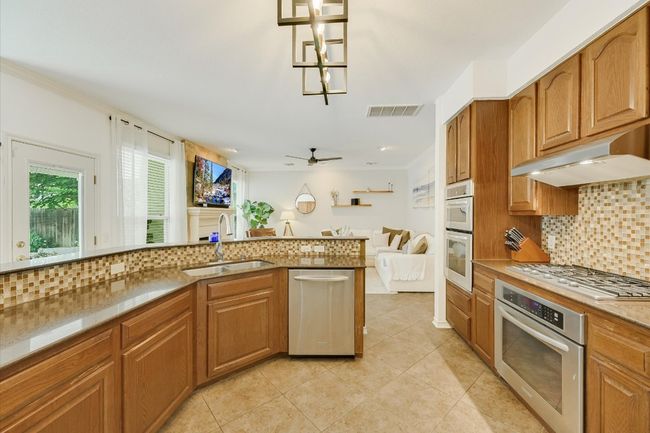 Kitchen with a sink, under cabinet range hood, appliances with stainless steel finishes, tasteful backsplash, and light tile patterned floors | Image 10