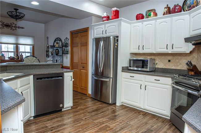 Kitchen featuring white cabinetry, wood finished floors, stainless steel appliances, dark countertops, and decorative backsplash | Image 7