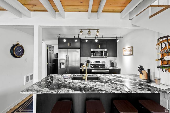 Kitchen with stainless steel appliances, dark cabinetry, a kitchen breakfast bar, a sink, and beam ceiling | Image 4