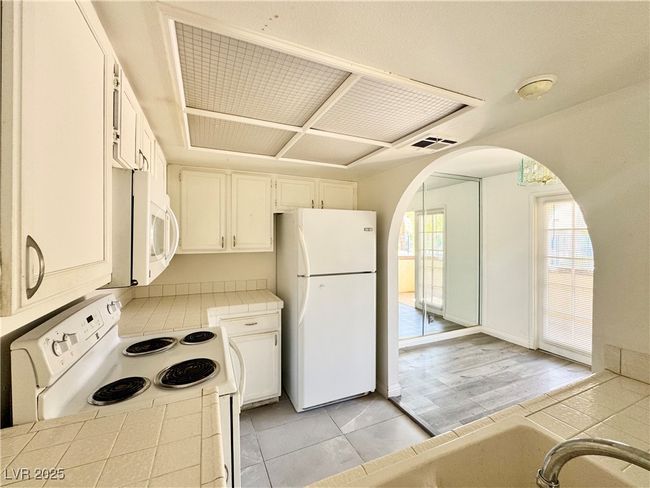 Kitchen featuring tile countertops, white appliances, arched walkways, white cabinets, and light tile patterned flooring | Image 8