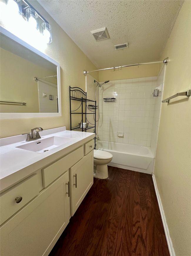 Bathroom featuring a textured ceiling, wood finished floors, shower / washtub combination, and vanity | Image 19