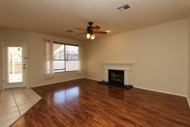 Unfurnished living room with wood finished floors, a fireplace with raised hearth, and a ceiling fan | Image 6