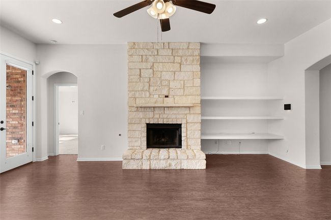 Unfurnished living room featuring built in shelves, dark wood-style floors, a ceiling fan, baseboards, and arched walkways | Image 23