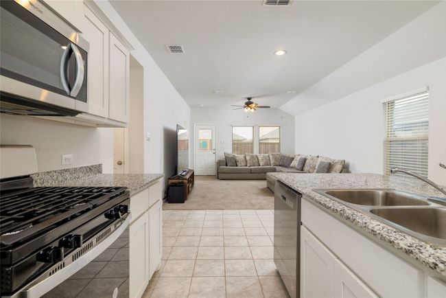 Kitchen with stainless steel appliances, light colored carpet, a sink, ceiling fan, and white cabinetry | Image 14