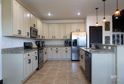 Kitchen with appliances with stainless steel finishes, light stone counters, pendant lighting, sink, and light tile floors | Image 3