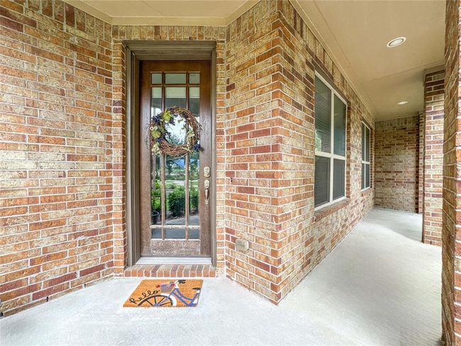 This photo showcases a welcoming brick entryway with a charming wooden front door, adorned with a decorative wreath and a colorful welcome mat. The area is well-lit and features a covered porch, offering a cozy and inviting entrance to the home. | Image 34