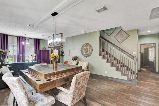 This photo showcases a stylish dining area, adjacent to a modern staircase. The room features elegant lighting, dark wood-look flooring, and vibrant curtains, creating a warm and inviting atmosphere. | Image 8