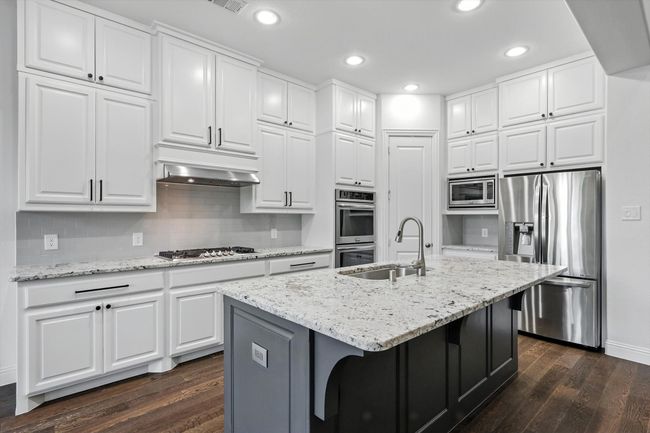 Kitchen featuring stainless steel appliances, dark wood-style flooring, white cabinets, recessed lighting, and light stone counters | Image 12