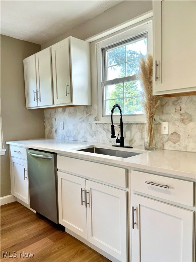 Kitchen featuring stainless steel dishwasher, white cabinetry, light countertops, and light wood finished floors | Image 7