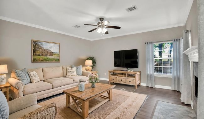 Living room with ceiling fan, crown molding, a fireplace, baseboards, and wood finished floors (vrtually staged) | Image 9