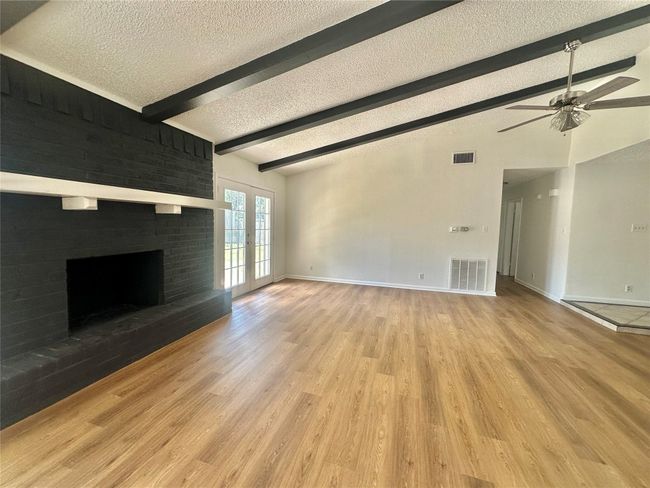 Unfurnished living room with a textured ceiling, french doors, ceiling fan, wood finished floors, and a fireplace | Image 9
