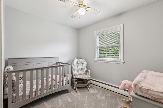 Carpeted bedroom featuring baseboard heating, ceiling fan, and a nursery area | Image 16