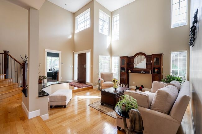 Living area with a healthy amount of sunlight, stairs, light wood-style floors, baseboards, and a high ceiling | Image 4