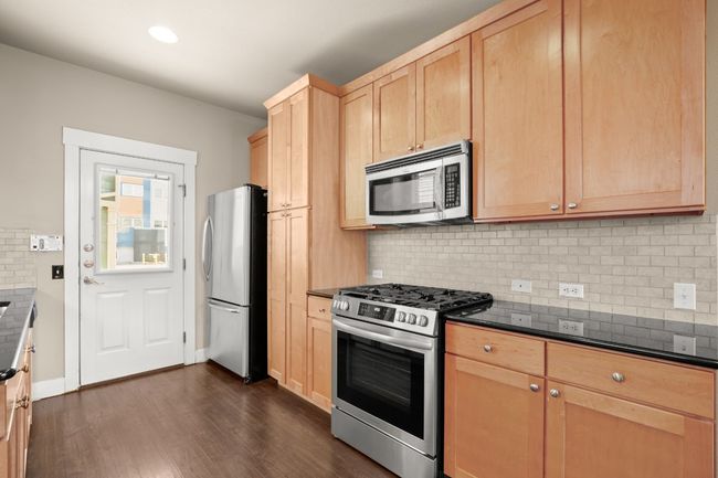 Kitchen with light brown cabinets, dark countertops, dark wood finished floors, stainless steel appliances, and decorative backsplash | Image 12