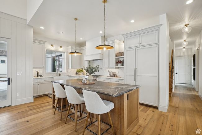 Kitchen with white cabinets, a kitchen island, a kitchen breakfast bar, hanging light fixtures, and light wood-type flooring | Image 13