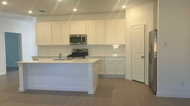 Kitchen with decorative backsplash, stainless steel appliances, white cabinetry, a kitchen island with sink, and recessed lighting | Image 7