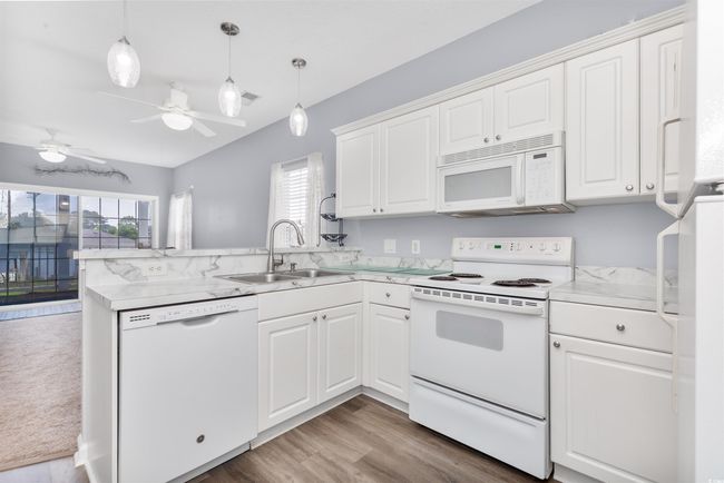 Kitchen with white appliances, a sink, a peninsula, white cabinetry, and light countertops | Image 6