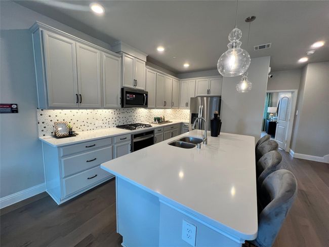 Kitchen with dark wood-style flooring, decorative backsplash, an island with sink, light countertops, and stainless steel appliances | Image 6
