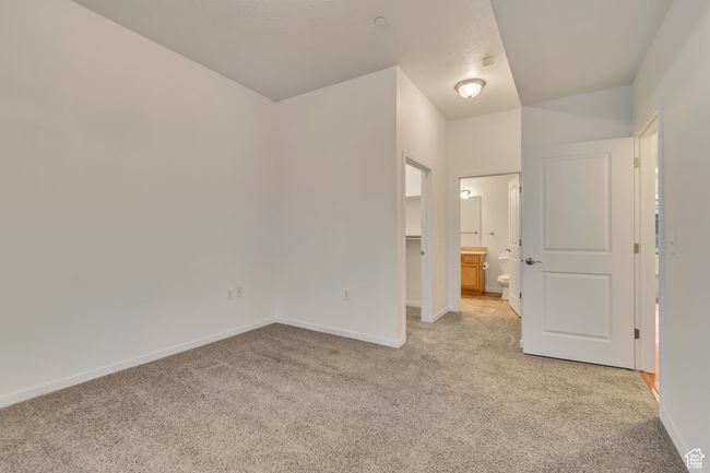 Unfurnished bedroom featuring a walk in closet, ensuite bathroom, baseboards, and light colored carpet | Image 17