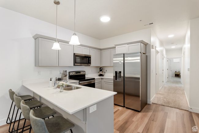 Kitchen featuring stainless steel appliances, a kitchen bar, a peninsula, light wood-style flooring, and light countertops | Image 5