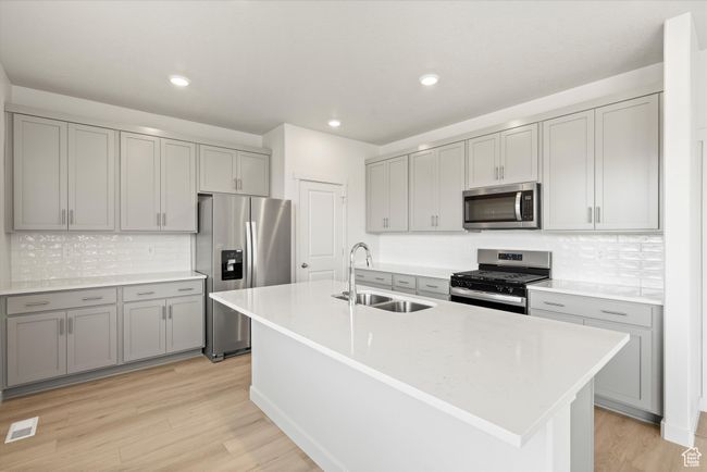 Kitchen featuring stainless steel appliances, gray cabinetry, tasteful backsplash, light wood-style flooring, and light countertops | Image 21