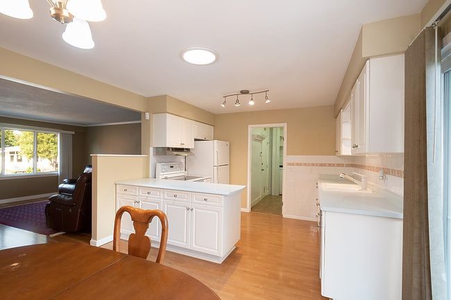 Kitchen with freestanding refrigerator, stove, white cabinets, light countertops, and a peninsula | Image 12