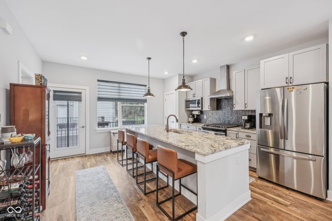 kitchen with a sink, backsplash, appliances with stainless steel finishes, a center island with sink, and wall chimney range hood | Image 8