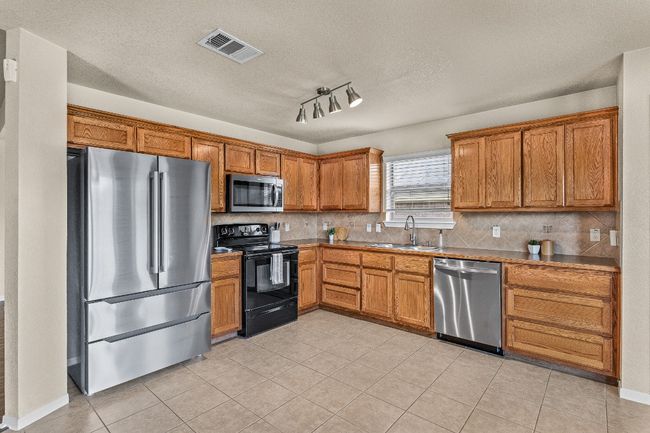 Kitchen with appliances with stainless steel finishes, light tile patterned floors, decorative backsplash, and a textured ceiling | Image 21