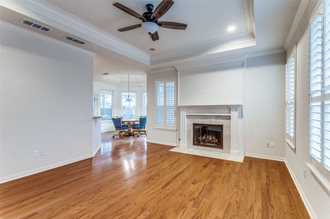 Family Room with a ceiling fan, light wood floors, a premium fireplace, crown molding, raised ceiling and plantation shutters. | Image 8