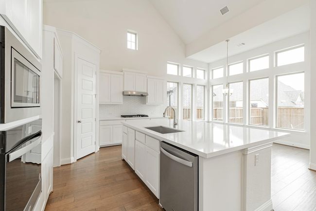 Kitchen featuring stainless steel appliances, a sink, high vaulted ceiling, light countertops, and hardwood / wood-style flooring | Image 6