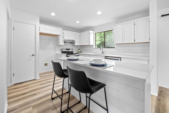 Kitchen with stainless steel range with electric stovetop, under cabinet range hood, white cabinetry, recessed lighting, and decorative backsplash | Image 8