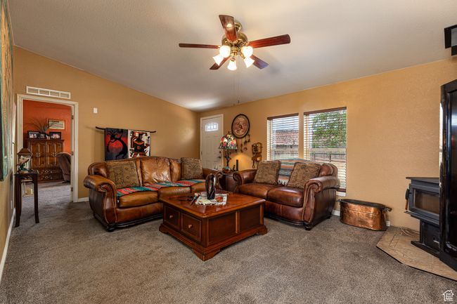 Living room with vaulted ceiling, carpet, ceiling fan, and a wood stove | Image 4