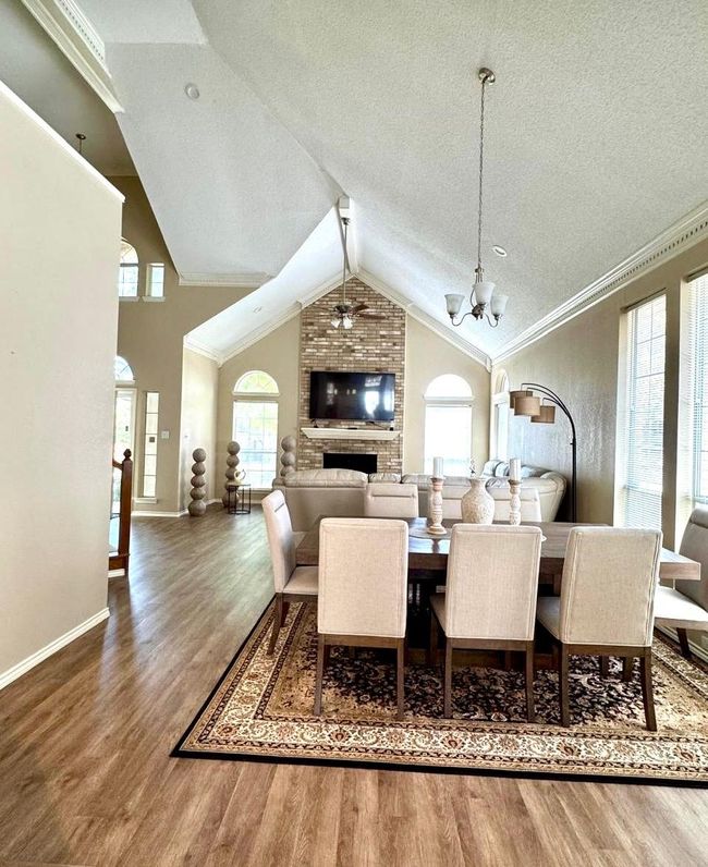 Dining room with ceiling fan with notable chandelier, a textured ceiling, ornamental molding, wood finished floors, and lofted ceiling | Image 6