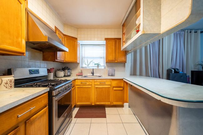 Kitchen with stainless steel gas range, a sink, extractor fan, light countertops, and light tile patterned floors | Image 13