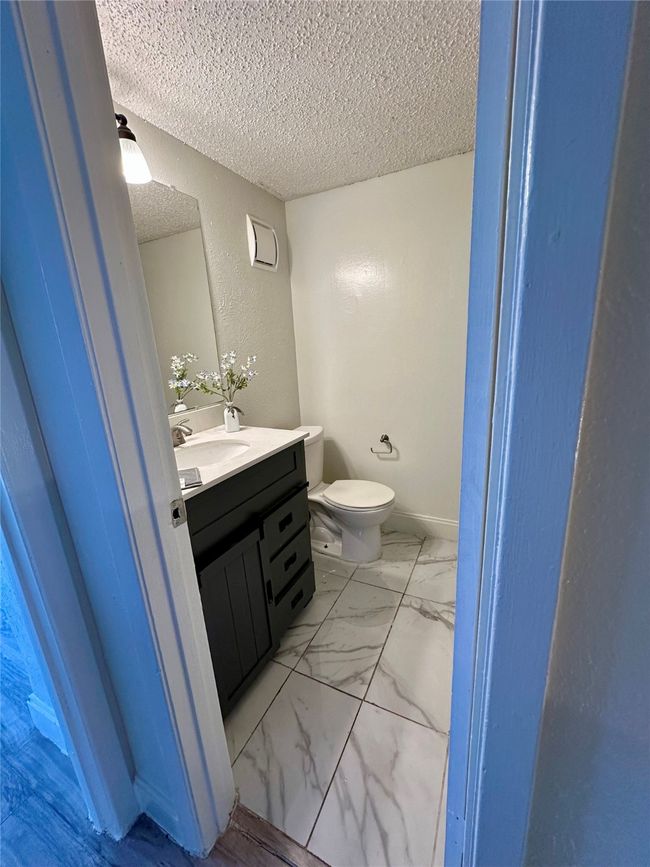 Half bathroom featuring a textured ceiling, vanity, toilet, marble look tile flooring, and a textured wall | Image 9