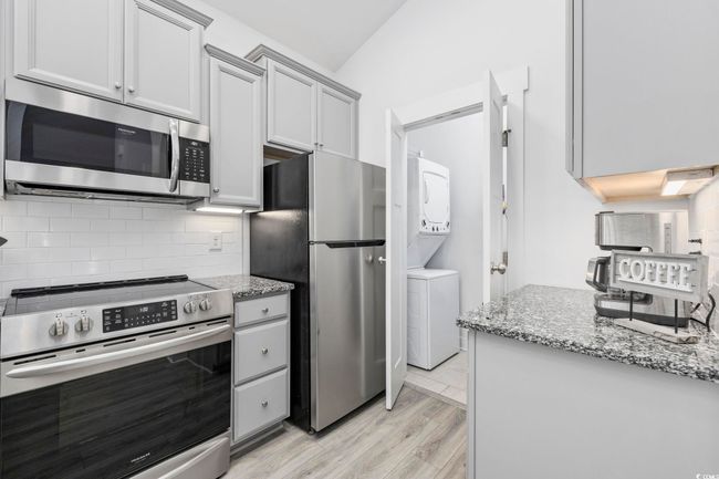 Kitchen featuring stainless steel appliances, light wood-style flooring, decorative backsplash, stacked washer and clothes dryer, and light stone countertops | Image 11