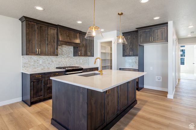 Kitchen with range with gas stovetop, dark brown cabinets, light wood finished floors, recessed lighting, and a textured ceiling | Image 8