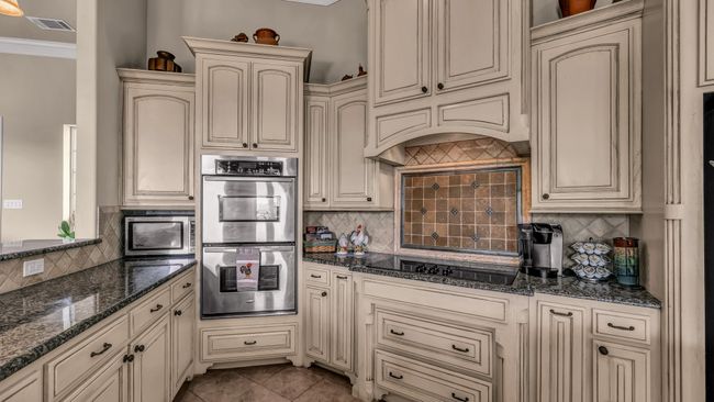 Kitchen with decorative backsplash, stainless steel double oven, black electric stovetop, and cream cabinetry | Image 15